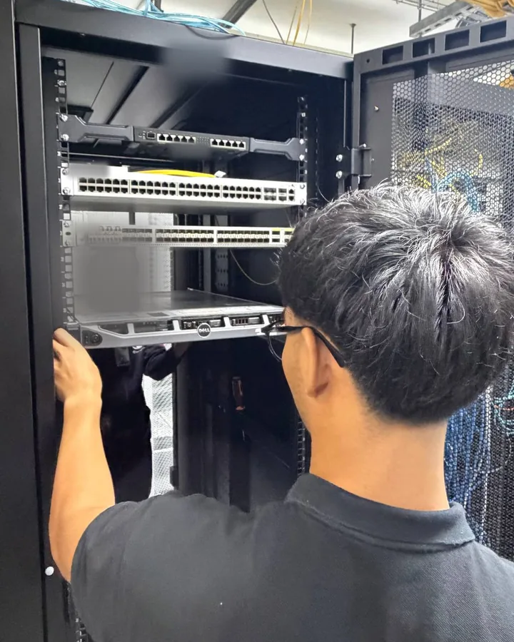 A team member, seen from behind, installing a server in a rack; labels are blurred